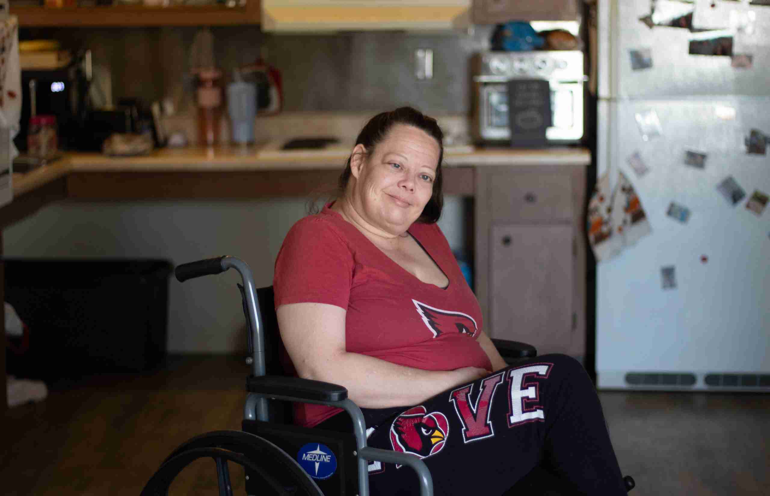 A woman sitting in her kitchen in her wheelchair repping Arizona Cardinals gear.