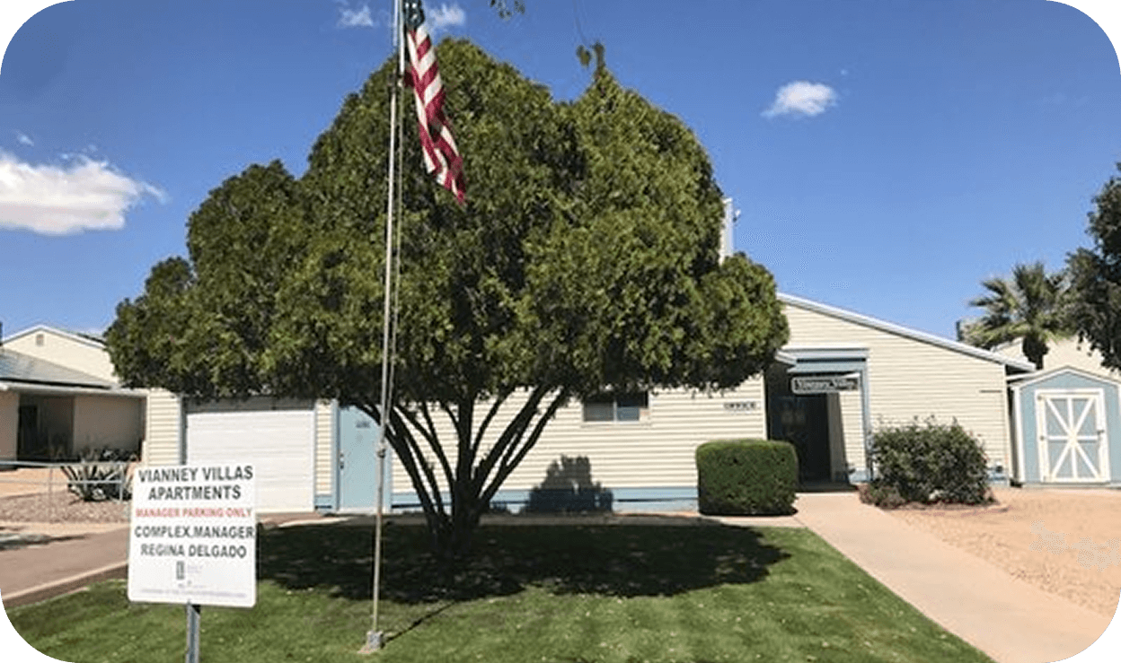Exterior of an apartment building with a large tree and flagpole in the front