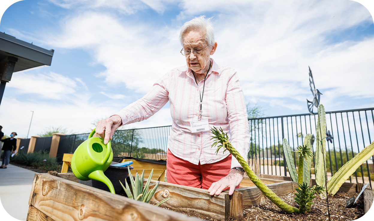 A woman using a watering can to water a garden bed